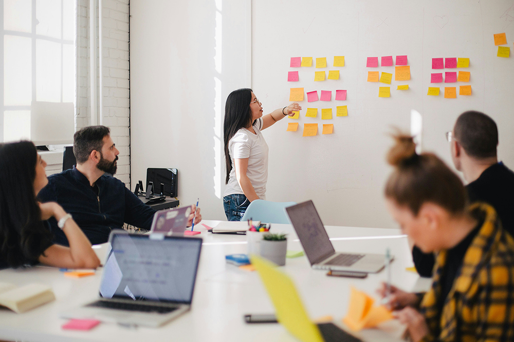 Team members meeting around a whiteboard with sticky notes.